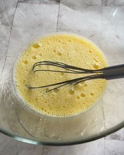 Una ciotola di vetro piena di liquido giallo e una frusta al suo interno.