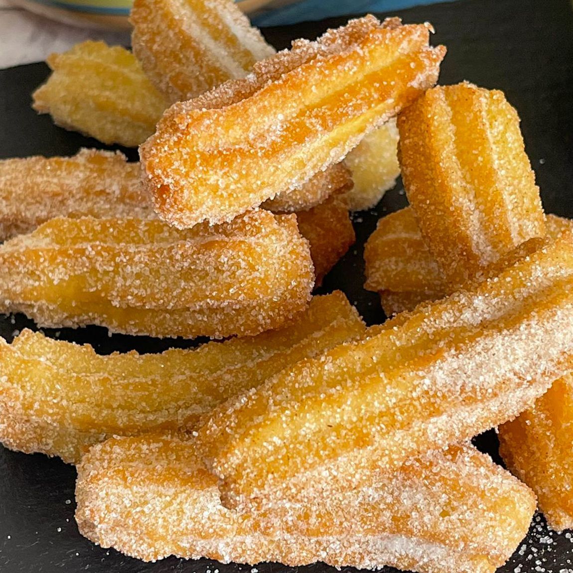 Una pila di churros ricoperti di zucchero su un piatto nero.
