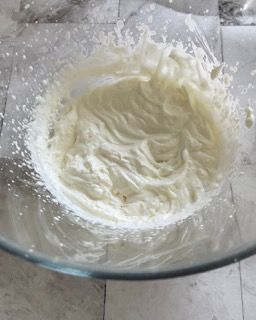 Una ciotola di vetro piena di panna montata su un tavolo.