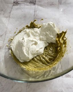 La panna montata viene aggiunta a una salsa verde in una ciotola di vetro.