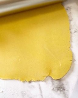 Un pezzo di pasta gialla viene steso su un tavolo.