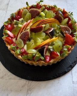 Una crostata di frutta con fragole e uva su un piatto nero