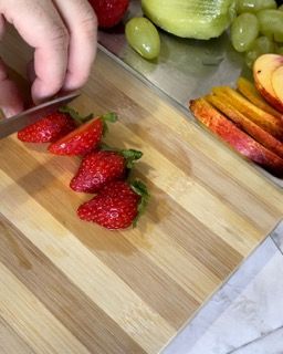 Una persona sta tagliando le fragole su un tagliere di legno.