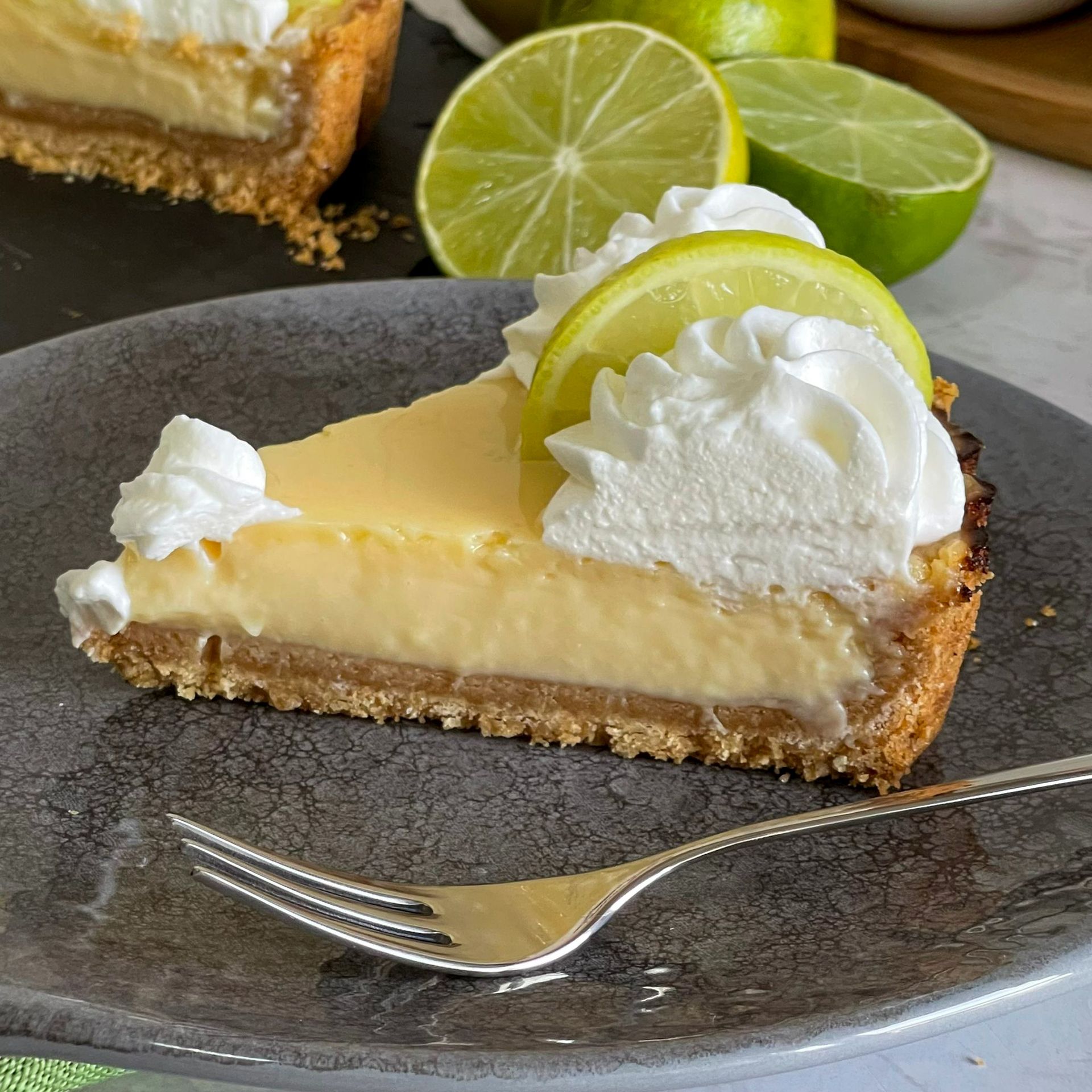Una fetta di torta al lime con panna montata e fette di lime su un piatto con una forchetta.