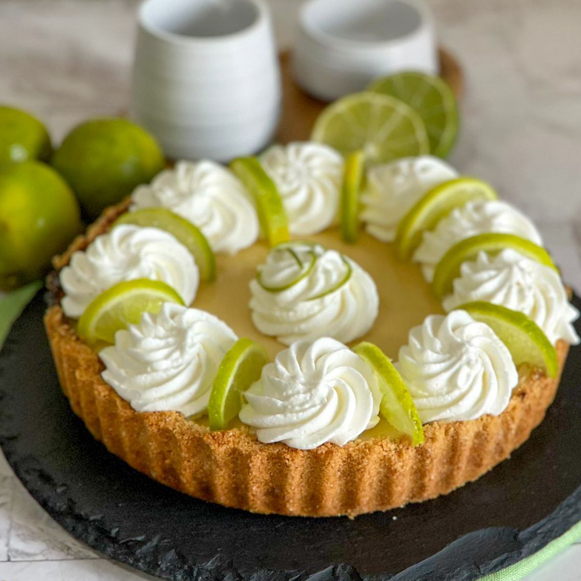 Una torta al lime con panna montata e fette di lime su un piatto nero.