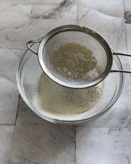 Una ciotola di farina viene setacciata attraverso un colino.