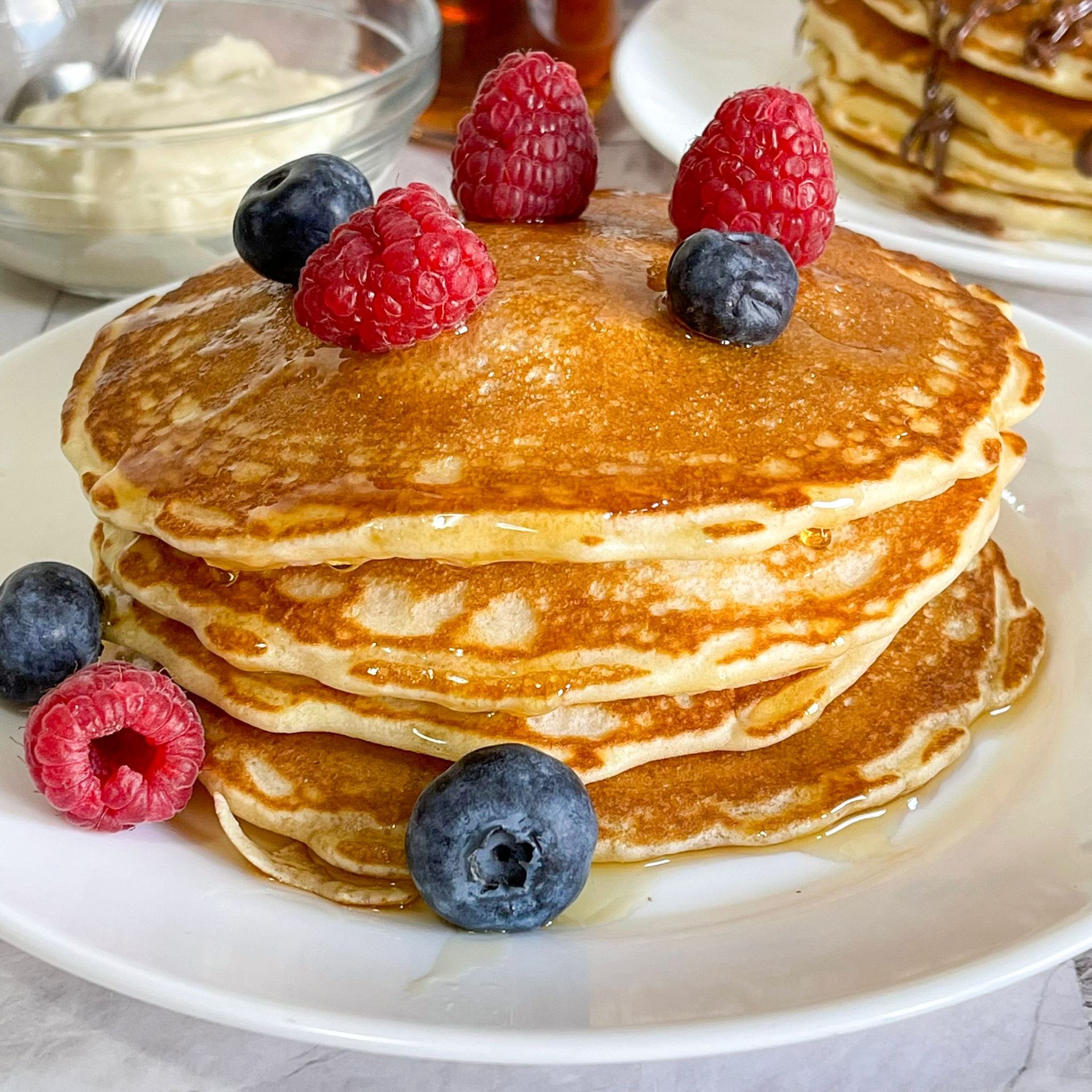 Una pila di pancake con lamponi e mirtilli sopra su un piatto bianco.