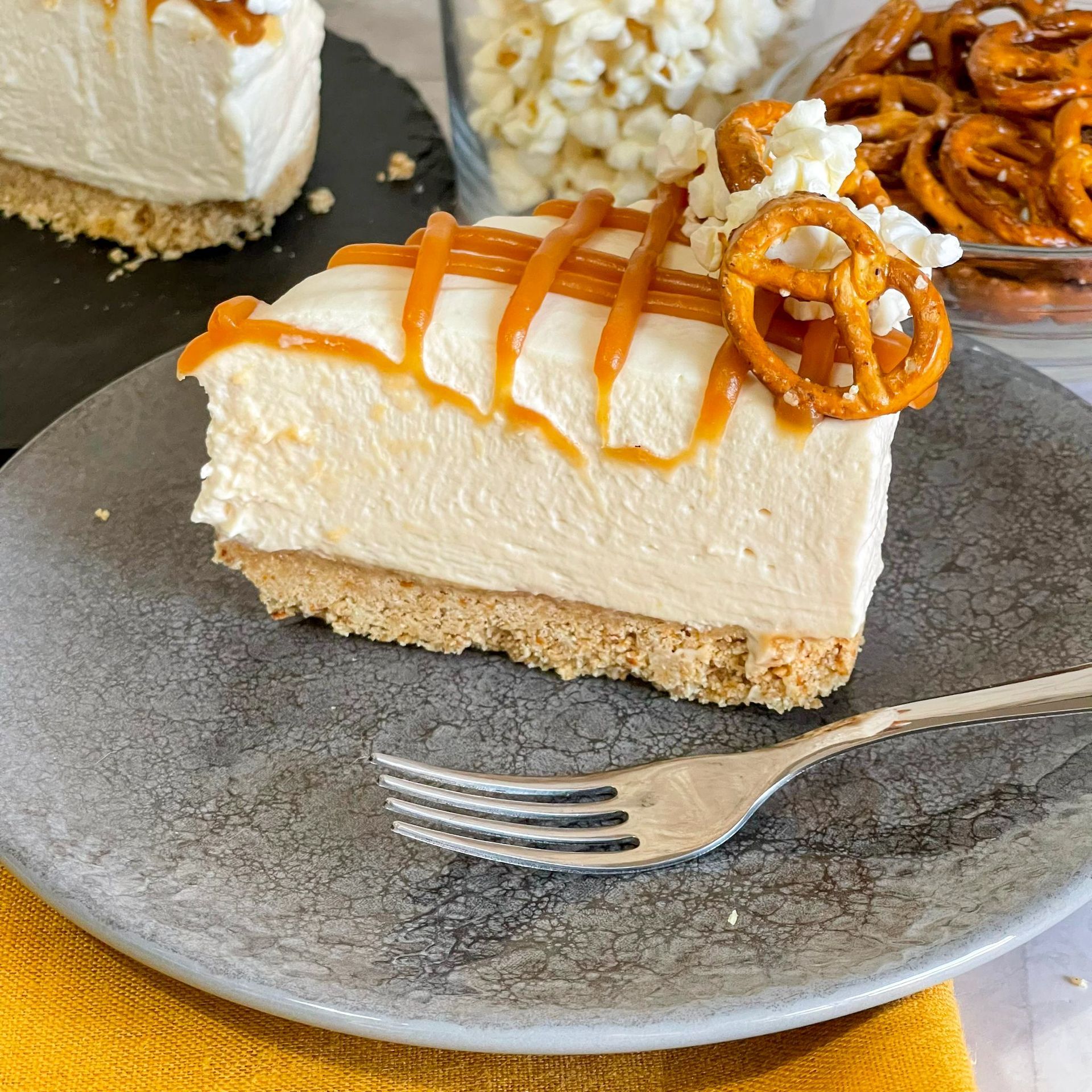 Un pezzo di cheesecake con pretzel e salsa al caramello su un piatto con una forchetta.