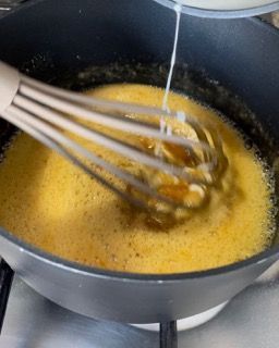 Si usa una frusta per mescolare un liquido giallo in una pentola.