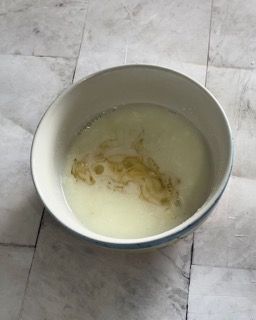 Una ciotola bianca piena di liquido è appoggiata su un tavolo.