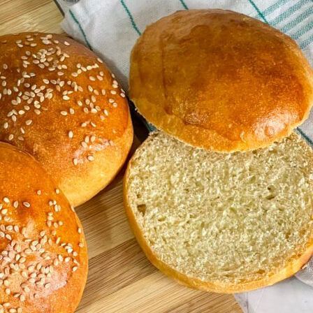 Tre panini per hamburger con semi di sesamo sono appoggiati su un tagliere di legno.