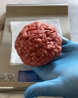 Una persona che indossa guanti blu tiene un pezzo di carne macinata davanti a una bilancia