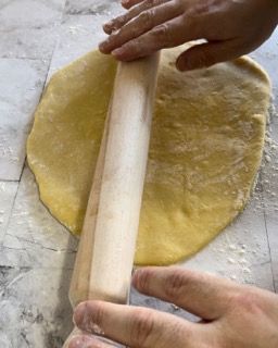 Una persona sta stendendo un pezzo di pasta con un mattarello.