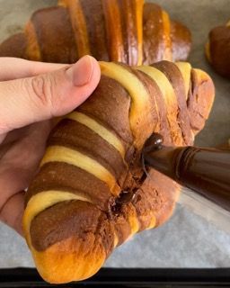 Una persona tiene in mano un croissant ricoperto di glassa al cioccolato.