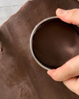Una persona sta usando uno stampino per biscotti per fare un buco in un pezzo di pasta al cioccolato.