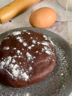Un pezzo di pasta al cioccolato su un piatto accanto a un uovo e un mattarello.