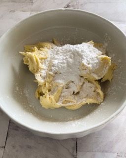 Una ciotola bianca piena di burro e zucchero a velo su un tavolo.