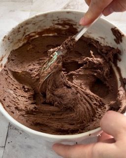 Una persona sta mescolando la glassa al cioccolato in una ciotola con una spatola.