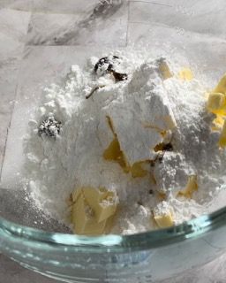 Una ciotola di vetro piena di zucchero a velo e burro.