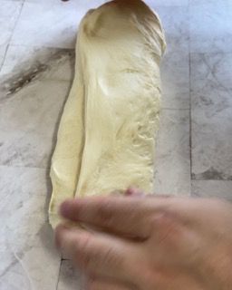 Una persona tiene in mano un pezzo di pasta su un tavolo.