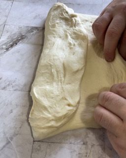 Una persona tiene in mano un pezzo di pasta su un tavolo.