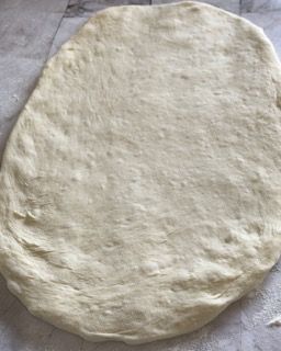 Un impasto per pizza è appoggiato su un foglio di carta oleata su un tavolo.