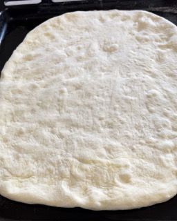 Un impasto per pizza è appoggiato su una padella nera.