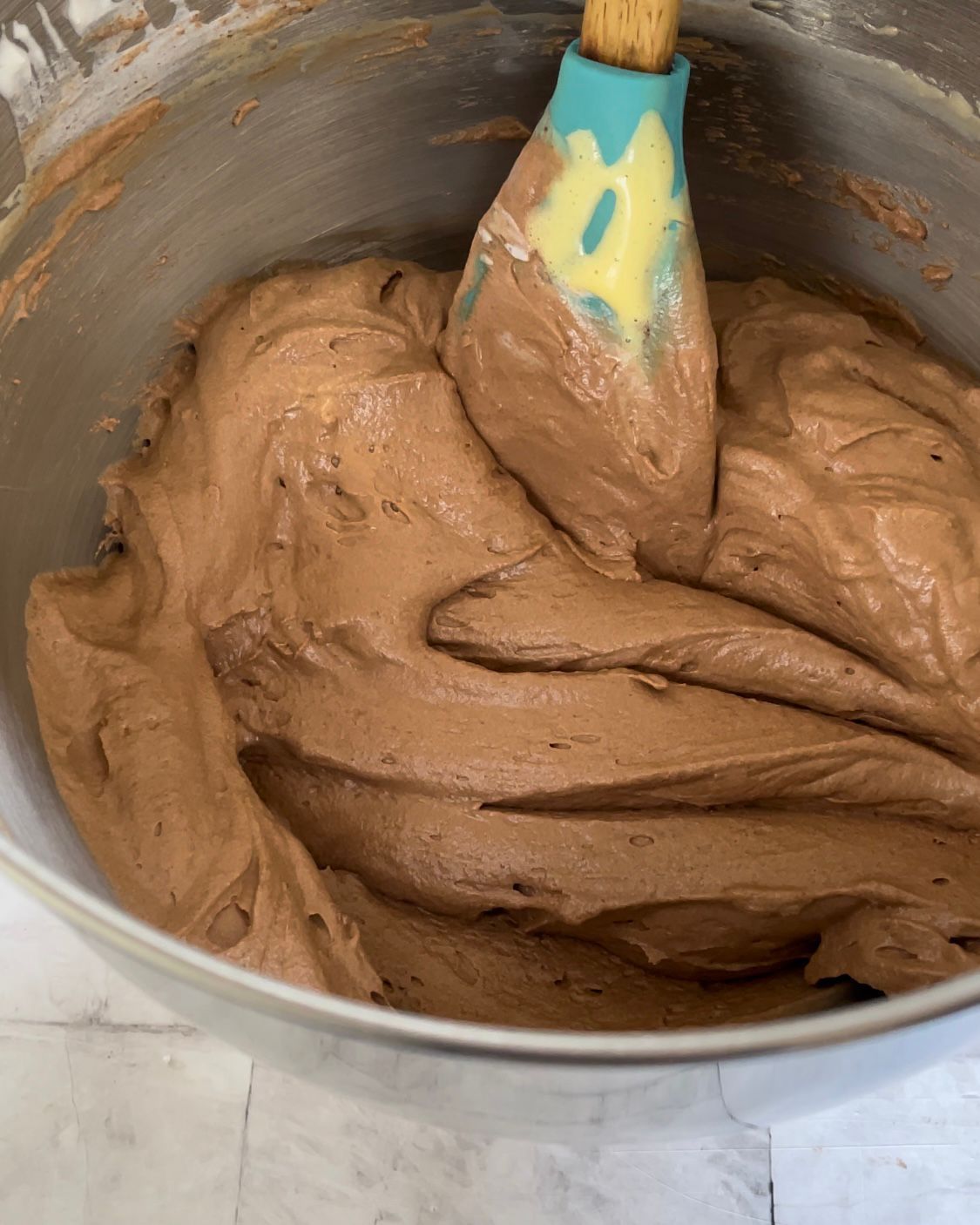 Una ciotola di glassa al cioccolato con una spatola dentro.