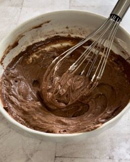 Una ciotola di glassa al cioccolato con una frusta dentro