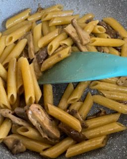 Una padella piena di pasta e funghi con una spatola blu