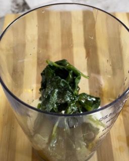 Una ciotola di foglie verdi è su un tagliere di legno.