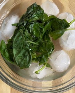 Una ciotola di spinaci e cubetti di ghiaccio su un tavolo di legno.