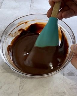 Una persona sta mescolando una ciotola di salsa al cioccolato con una spatola blu