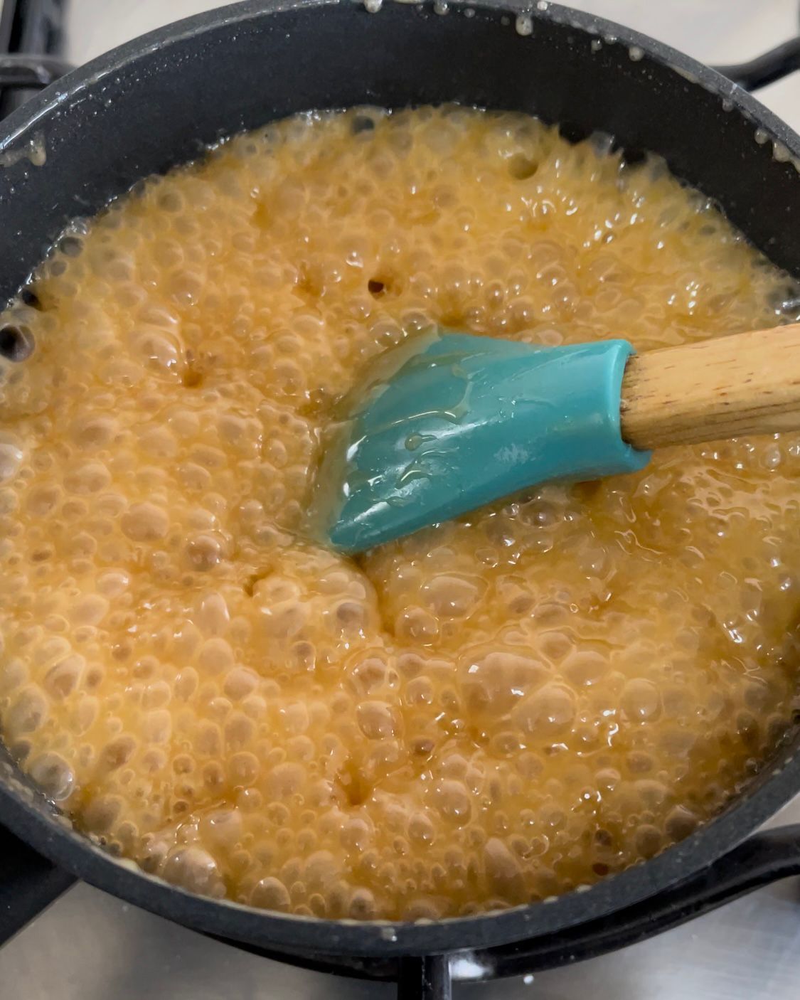 Una spatola blu viene utilizzata per mescolare un liquido marrone in una padella.