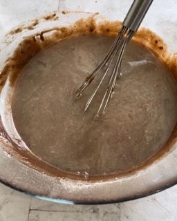 Una ciotola di liquido marrone con una frusta dentro