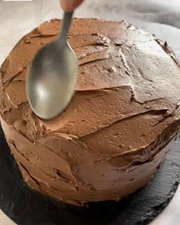 Una persona sta usando un cucchiaio per spalmare la glassa al cioccolato su una torta