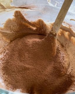 Un cucchiaio di legno è in una ciotola di cioccolato in polvere.