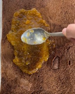 Una persona sta usando un cucchiaio per spalmare la marmellata su una fetta di torta al cioccolato.