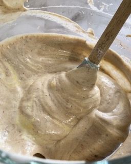 Un primo piano di una ciotola di salsa con un cucchiaio di legno dentro.
