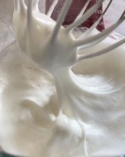 Primo piano di una frusta in una ciotola di panna montata.