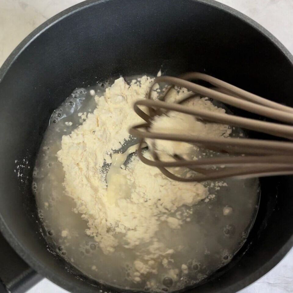 Una frusta è in una pentola di liquido con farina
