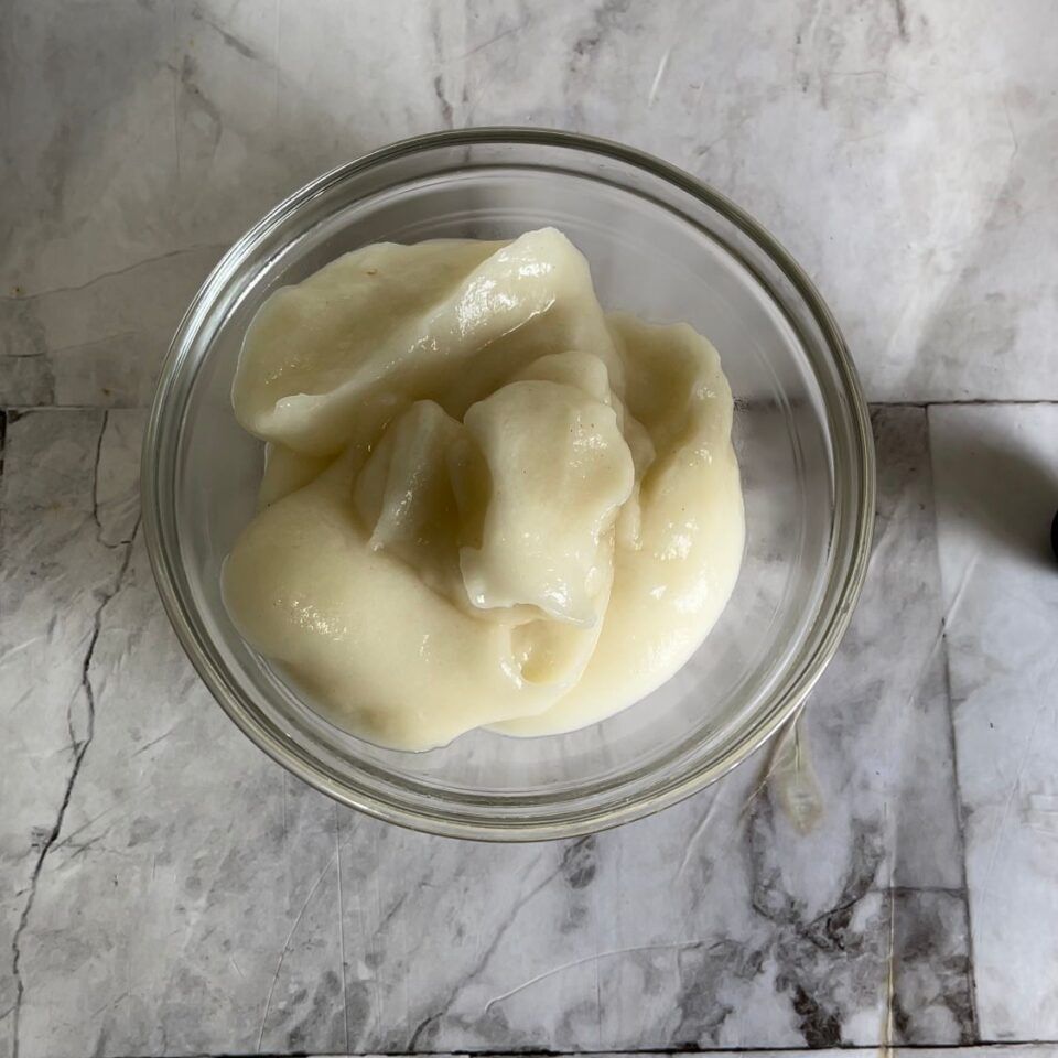 Una ciotola di vetro piena di liquido bianco su una superficie di marmo.