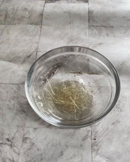 Una ciotola di vetro piena di liquido è appoggiata su un pavimento piastrellato.