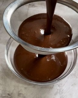 Una ciotola di salsa al cioccolato viene versata attraverso un colino.