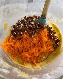 Una ciotola di carote e noci pecan con una spatola dentro.