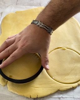 Una persona che indossa un braccialetto sta tagliando un cerchio da un pezzo di pasta