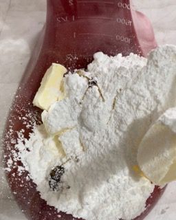 Una tazza graduata rossa piena di zucchero a velo e burro