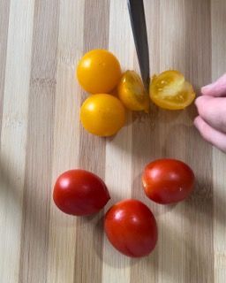 Una persona sta tagliando i pomodorini su un tagliere di legno.