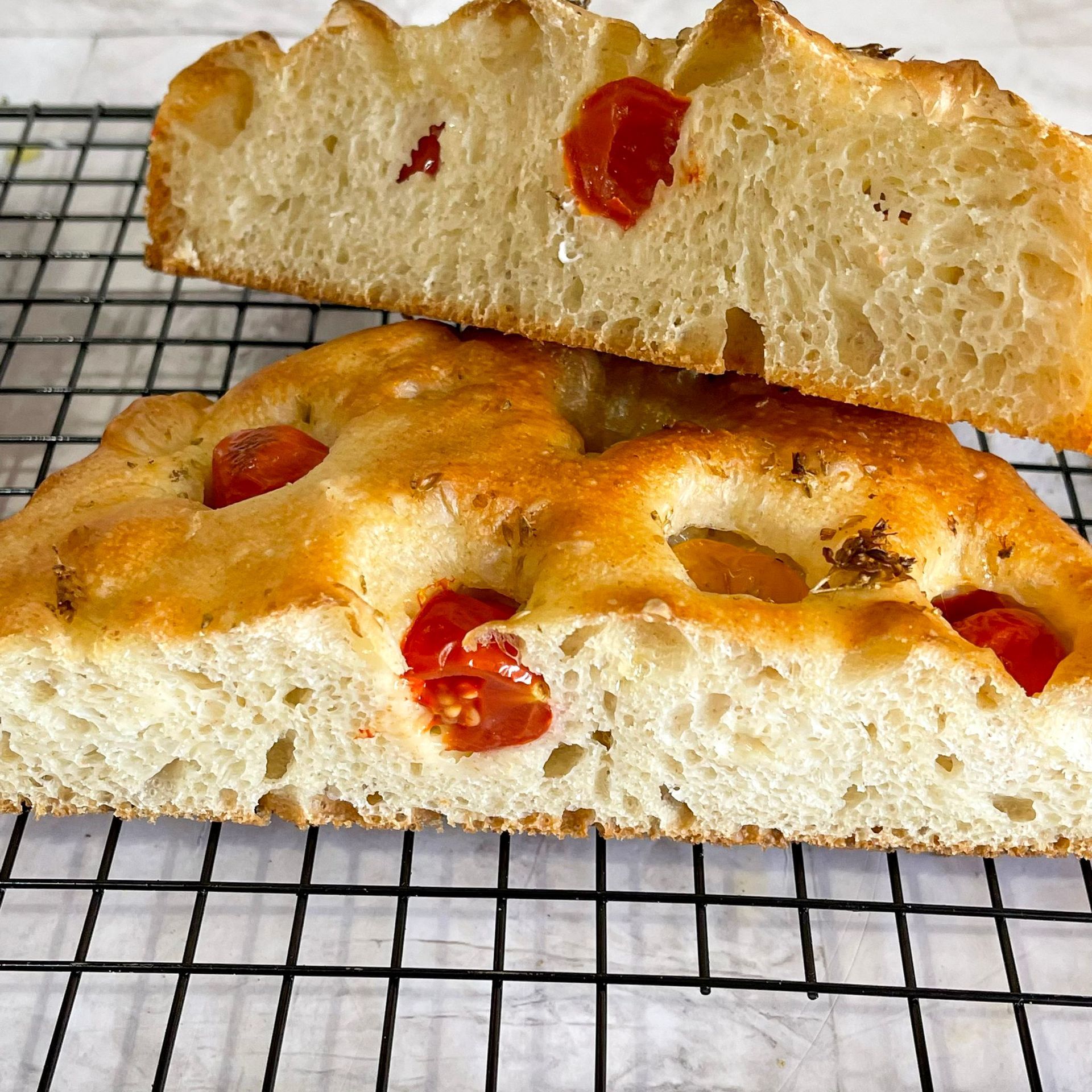 Due fette di pane con sopra dei pomodori sono adagiate una sopra l'altra su una griglia di raffreddamento.