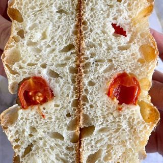 Una persona tiene in mano un pezzo di pane con dentro dei pomodori